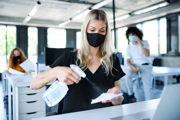 Jeune femme avec masque facial de retour au travail au bureau après verrouillage, les mains désinfectantes . — Photo