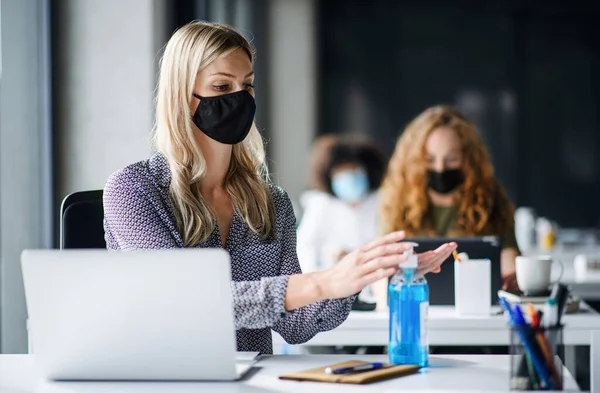 Jovem com máscara facial de volta ao trabalho no escritório após o bloqueio, desinfetando as mãos . — Fotografia de Stock