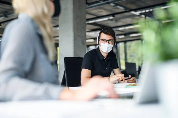 Jovens com máscaras faciais de volta ao trabalho no escritório após bloqueio, conversando . — Fotografia de Stock