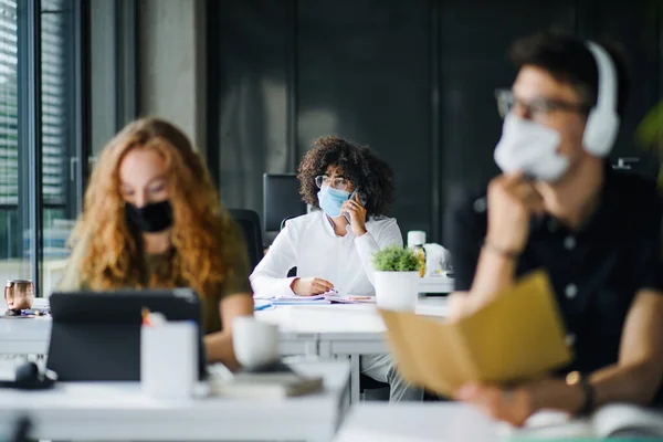 Unga människor med ansiktsmasker tillbaka på jobbet eller skolan på kontoret efter nedstängning. — Stockfoto