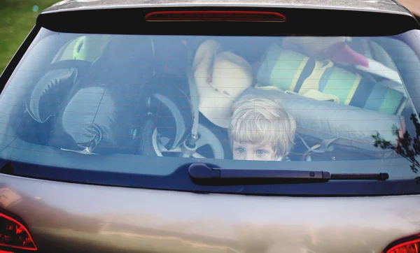 Small boy sitting in loaded car boot with closed door, local trip concept. — Stock Photo, Image