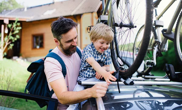 Vater mit kleinem Sohn stellt Fahrräder aufs Autodach und geht auf Ausflugsfahrt. — Stockfoto