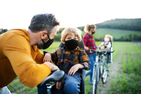 Család két kisgyerekkel kerékpártúrán, arcmaszkot viselve. — Stock Fotó