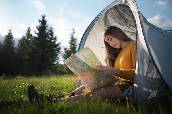 Szczęśliwa młoda kobieta siedzi w namiocie schronisko na świeżym powietrzu w letniej przyrody, za pomocą mapy. — Zdjęcie stockowe