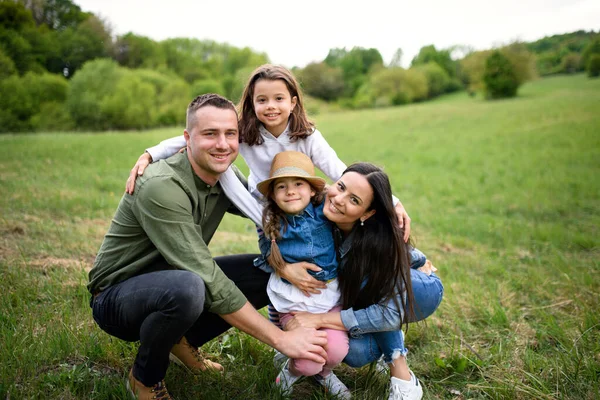 Famiglia felice con due piccole figlie sedute all'aperto nella natura primaverile, guardando la macchina fotografica . — Foto Stock