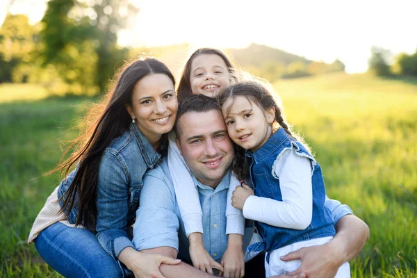 Familia feliz con dos hijas pequeñas sentadas al aire libre en la naturaleza de primavera, mirando a la cámara . — Foto de Stock