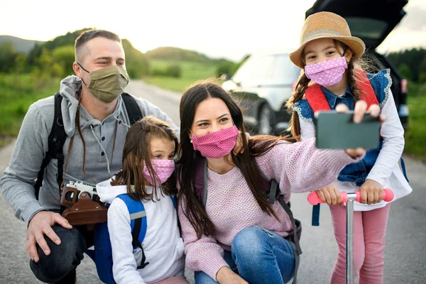 Famiglia con due piccole figlie e maschere per il viso in viaggio all'aria aperta nella natura, scattando selfie . — Foto Stock