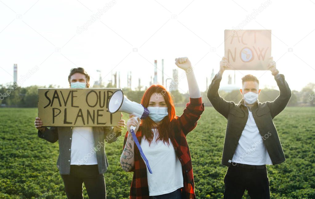 Group of young activists with placards standing outdoors by oil refinery, protesting.