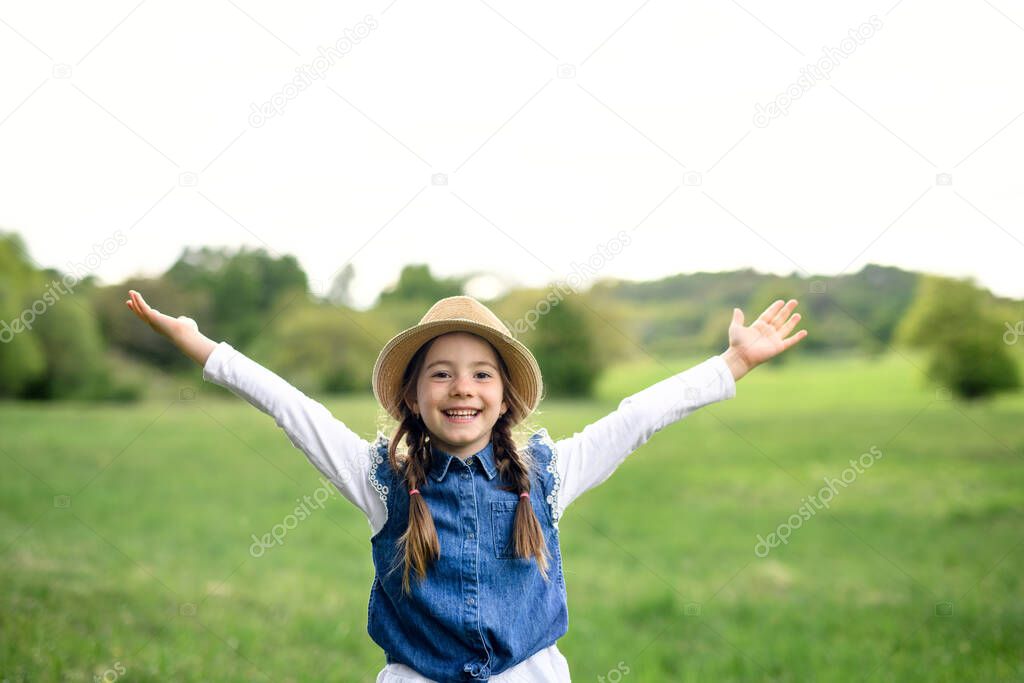 Portrait of small girl standing outdoors in spring nature, looking at camera.