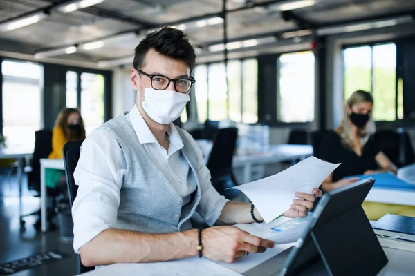 Portret van een jonge man met gezichtsmasker weer aan het werk na lockdown. — Stockfoto