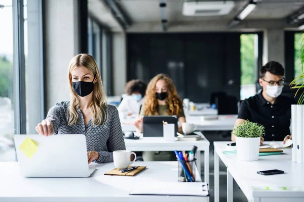 Młodzi ludzie w maskach twarzy z powrotem w pracy lub w szkole w biurze po zamknięciu. — Zdjęcie stockowe