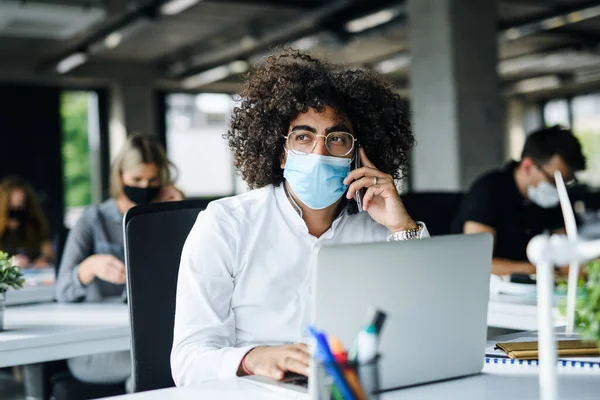 Portret van een jonge man met gezichtsmasker weer aan het werk na lockdown. — Stockfoto