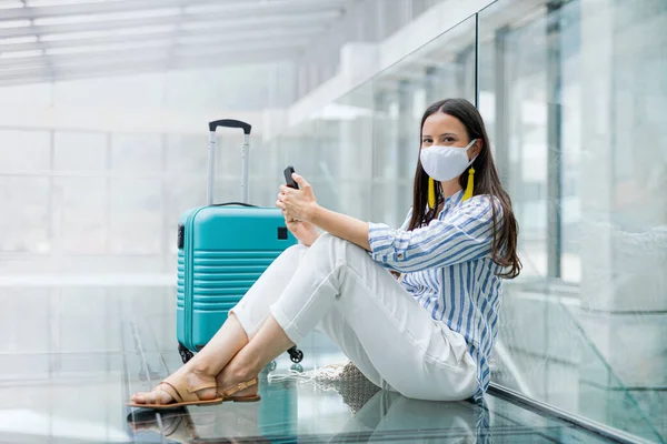 Giovane donna con smartphone che va in vacanza, indossa maschere facciali in aeroporto . — Foto Stock