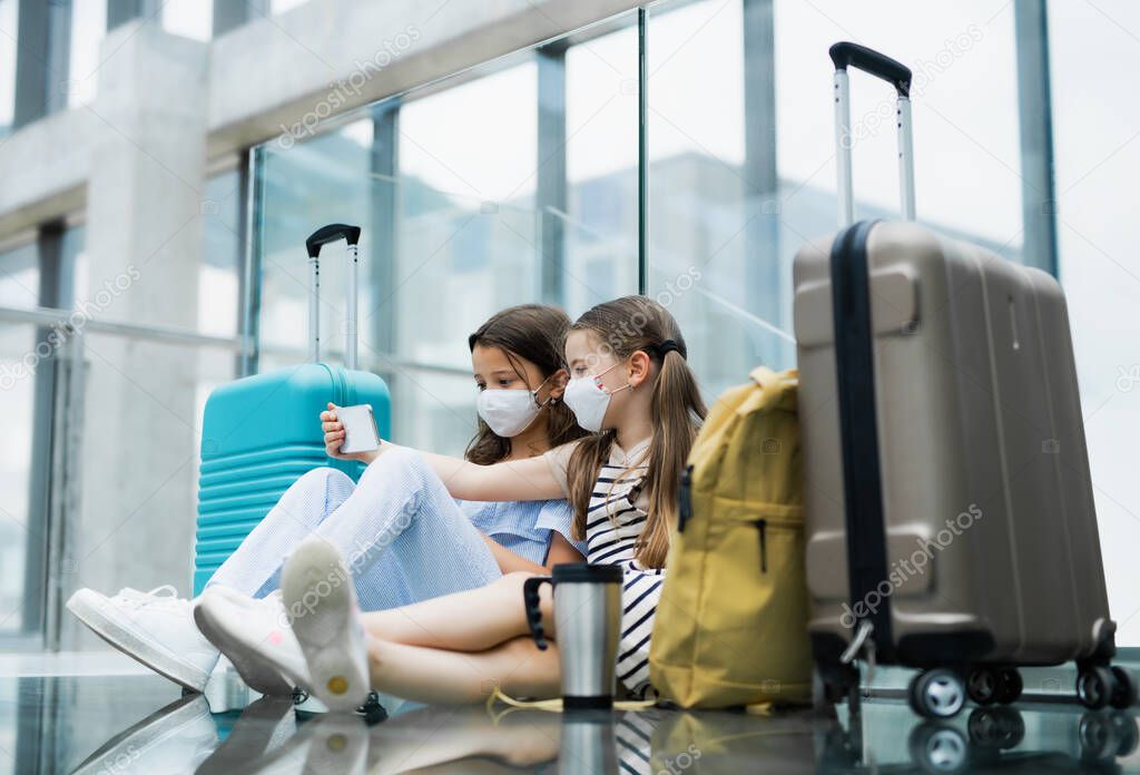 Small children with smartphone going on holiday, wearing face masks at the airport.