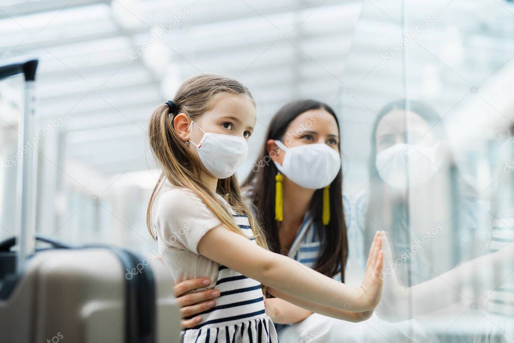 Mother with daughter going on holiday, wearing face masks at the airport.