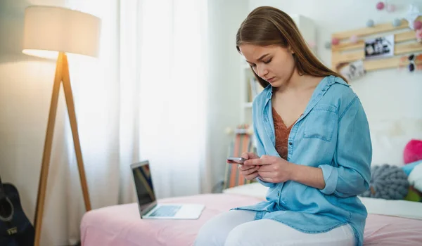 Tråkig och orolig ung flicka med smartphone sitter inomhus, internet missbruk koncept. — Stockfoto