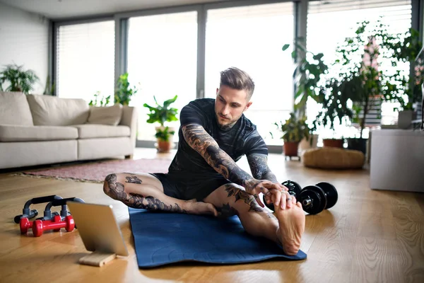 Vooraanzicht portret van de mens met tablet doet workout oefening binnen thuis. — Stockfoto