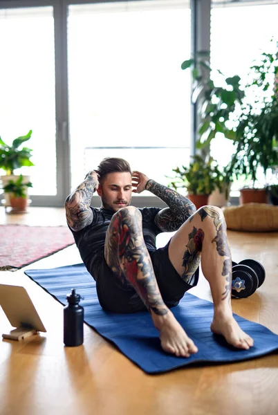 Vooraanzicht portret van de mens met tablet doet workout oefening binnen thuis. — Stockfoto