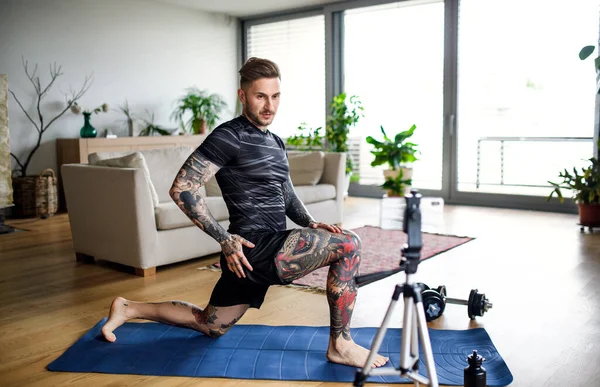 Man trainer doet online workout oefening binnen thuis, met behulp van camera. — Stockfoto