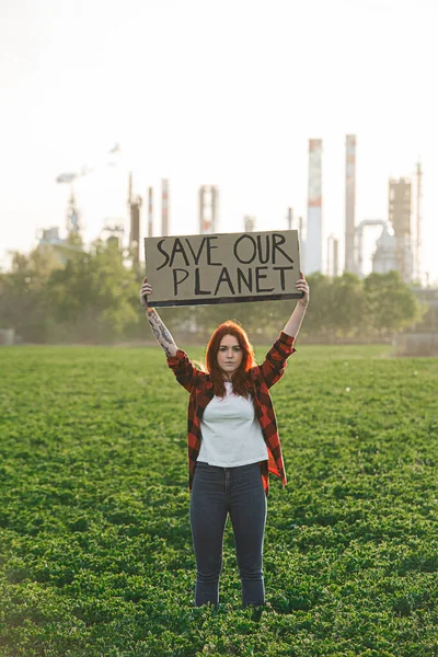 Giovane attivista donna con cartello in piedi all'aperto vicino alla raffineria di petrolio, protestando . — Foto Stock