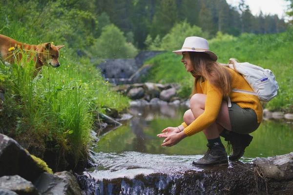 Gelukkig jong vrouw met hond staan door stroom op een wandeling buiten in de zomer natuur. — Stockfoto