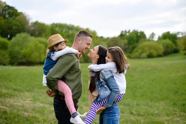 Familia feliz con dos hijas pequeñas de pie al aire libre en la naturaleza de primavera . —  Fotos de Stock