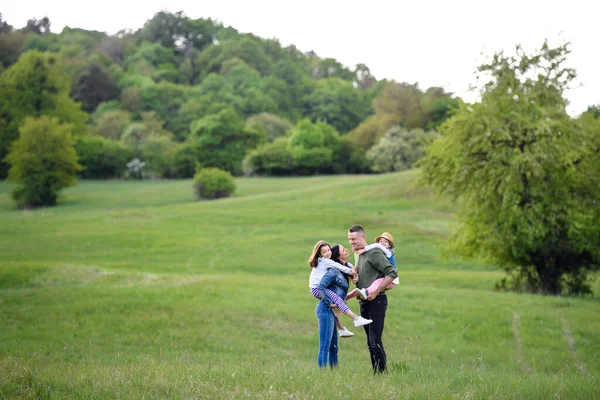 Famille heureuse avec deux petites filles debout à l'extérieur dans la nature printanière. — Photo