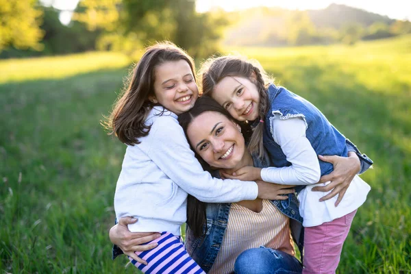 Madre con due piccole figlie che si divertono all'aperto nella natura primaverile, abbracciandosi . — Foto Stock