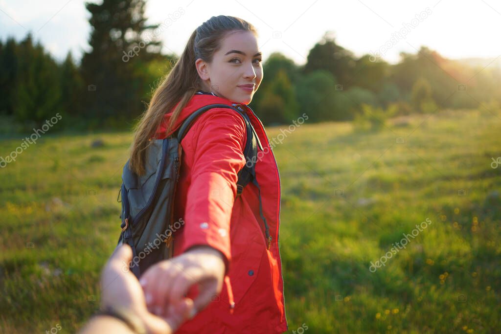 Young woman with backpack in summer nature, looking over shoulder at man.