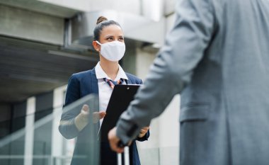 Uçuş görevlisi havaalanında tanınmayan bir işadamıyla konuşuyor, maske takıyor..