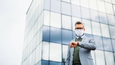 Açık havada duran, havaalanında maske takan işadamının alçak açılı görüntüsü..