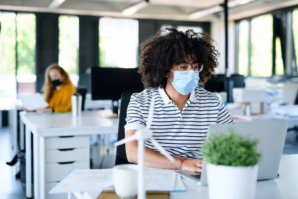 Portret van een jonge man met gezichtsmasker weer aan het werk na lockdown. — Stockfoto