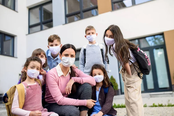 Grupo de crianças, professor com máscaras faciais ao ar livre na escola após o bloqueio covid-19 . — Fotografia de Stock