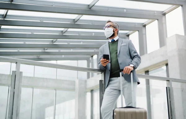 Empresario con equipaje en viaje de negocios, con mascarilla en el aeropuerto . — Foto de Stock