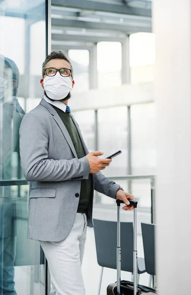 Businessman with luggage going on business trip, wearing face mask at the airport. — Stock Photo, Image
