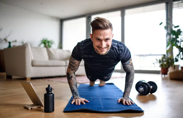 Vooraanzicht portret van de mens met tablet doet workout oefening binnen thuis. — Stockfoto