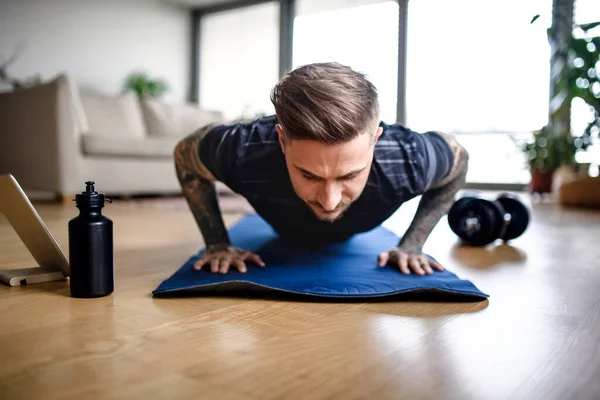 Vooraanzicht portret van de mens met tablet doet workout oefening binnen thuis. — Stockfoto