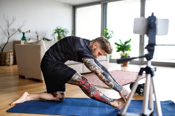 Man trainer doet online workout oefening binnen thuis, met behulp van camera. — Stockfoto