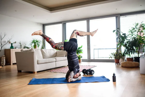 Jongeman doet workout oefening binnen thuis, headstand. — Stockfoto