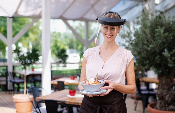 Waitress with protective face shield serving customers outdoors on terrace restaurant. — Stock Photo, Image