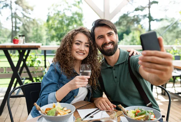 Casal feliz sentado ao ar livre no restaurante terraço, tirando selfie . — Fotografia de Stock