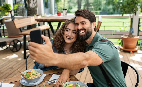 Szczęśliwa para siedzi na zewnątrz na tarasie restauracja, biorąc selfie. — Zdjęcie stockowe