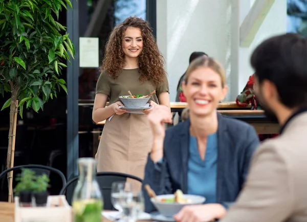 Waitress with face mask serving happy couple outdoors on terrace restaurant. — Stock Photo, Image