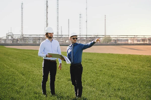 Dva mladí inženýři stojí venku u ropné rafinérie a diskutují o problémech. — Stock fotografie