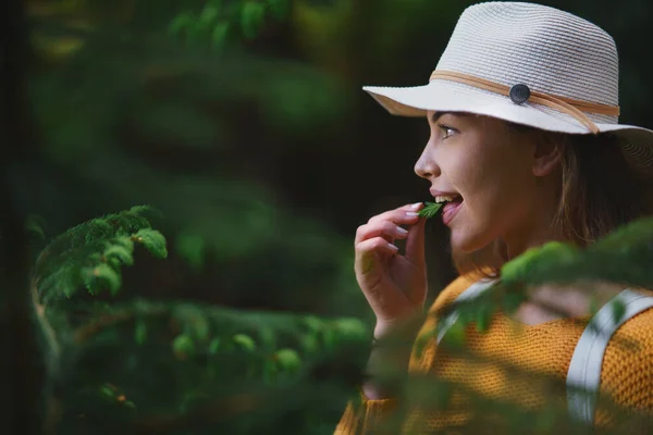 Giovane donna su una passeggiata all'aperto nella foresta nella natura estiva, mangiare germogli di abete rosso. — Foto Stock