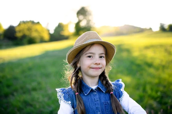Portret van een klein meisje dat in de lente in de natuur staat, kijkend naar de camera. — Stockfoto