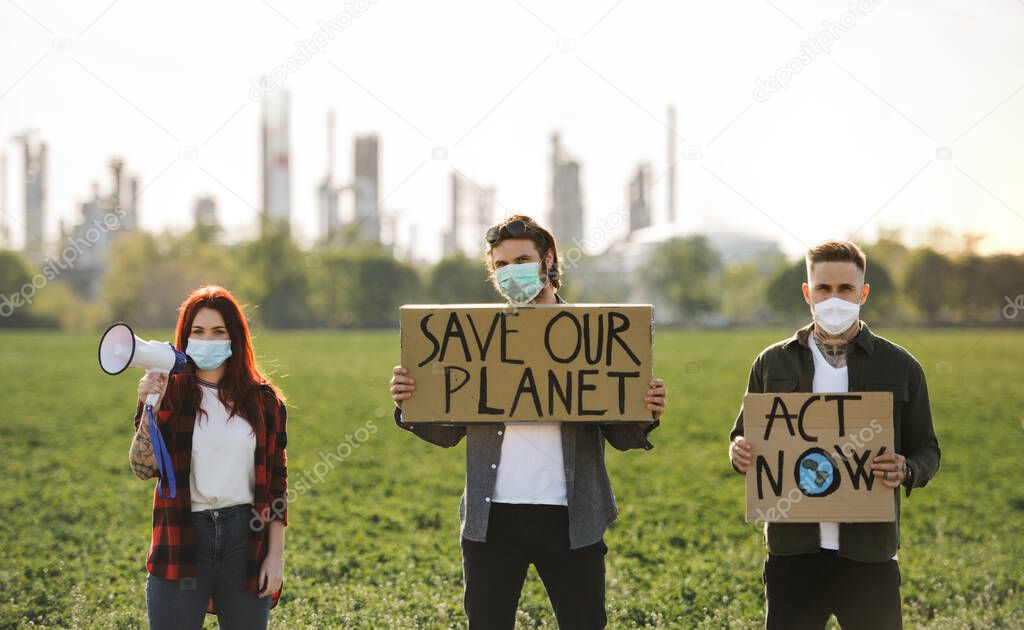 Group of young activists with placards standing outdoors by oil refinery, protesting.