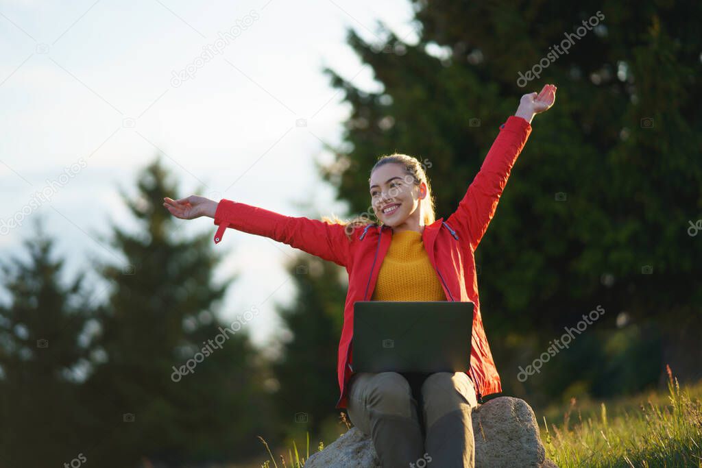 Happy young woman using laptop in summer nature, outdoor office concept.