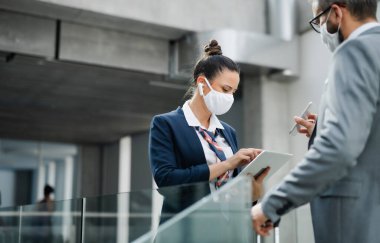 Uçuş görevlisi havaalanında iş adamıyla konuşuyor, maske takıyor..