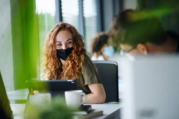 Mladá žena s obličejovou maskou zpět v práci v úřadu po uzamčení. — Stock fotografie